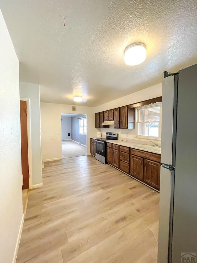 735 Poplar Ave, Las Animas, CO 81054 - kitchen with stainless steel appliances, light wood finished floors, light countertops, a textured ceiling, and under cabinet range hood