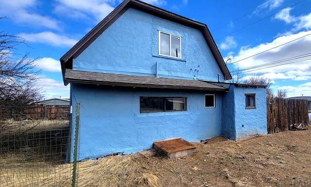 back of property with a shingled roof, fence, and stucco siding