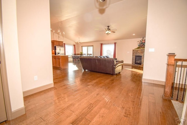 5707 Mark Twain Ln, Pueblo, CO 81008 - living room featuring light wood-type flooring, a ceiling fan, vaulted ceiling, a stone fireplace, and a chandelier