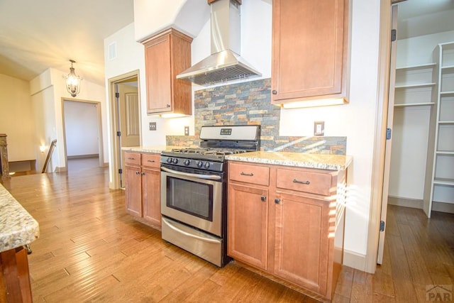 5707 Mark Twain Ln, Pueblo, CO 81008 - kitchen with stainless steel gas range, wall chimney range hood, light wood-style flooring, tasteful backsplash, and light stone counters