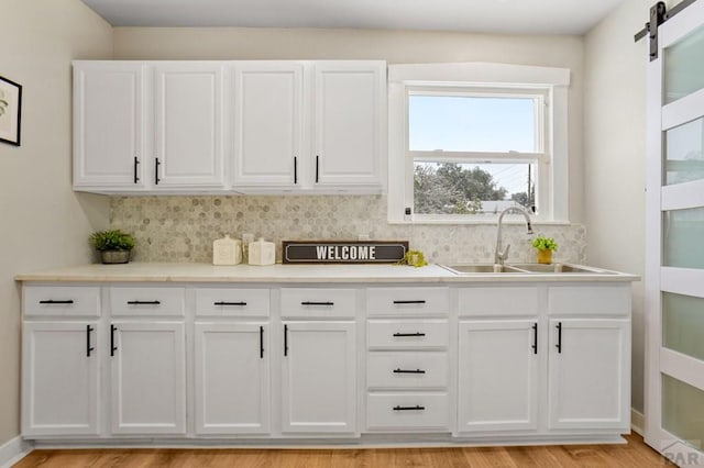 kitchen featuring a barn door, white cabinets, decorative backsplash, light countertops, and a sink