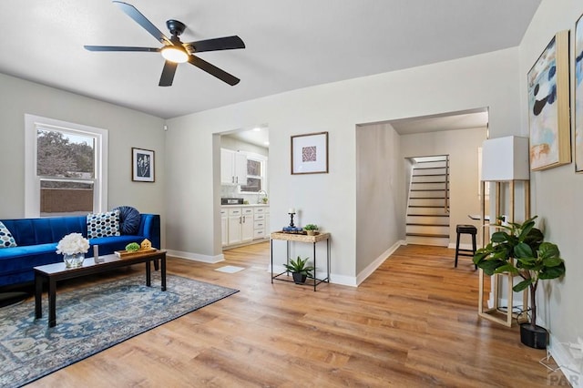 living area with ceiling fan, stairway, light wood-type flooring, and baseboards