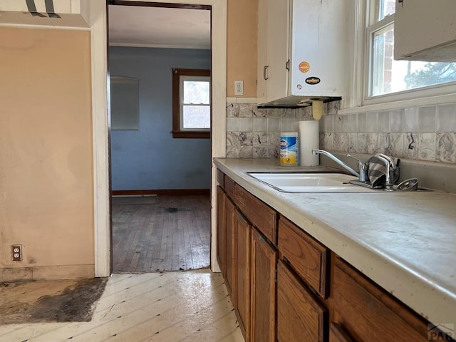 kitchen with light wood finished floors, baseboards, brown cabinetry, light countertops, and a sink