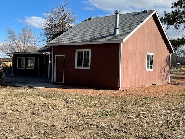 rear view of house with roof with shingles and a patio area