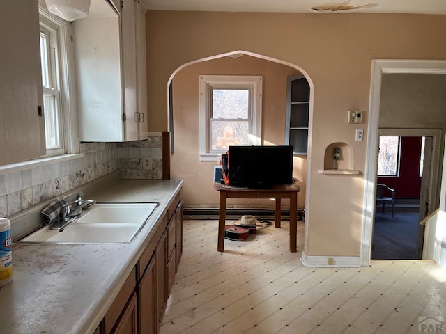 kitchen with light wood finished floors, tasteful backsplash, brown cabinetry, light countertops, and a sink