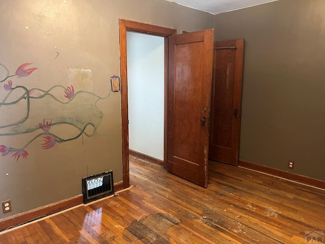 empty room featuring hardwood / wood-style floors, visible vents, and baseboards