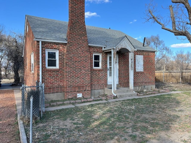 bungalow with roof with shingles, brick siding, a chimney, and fence