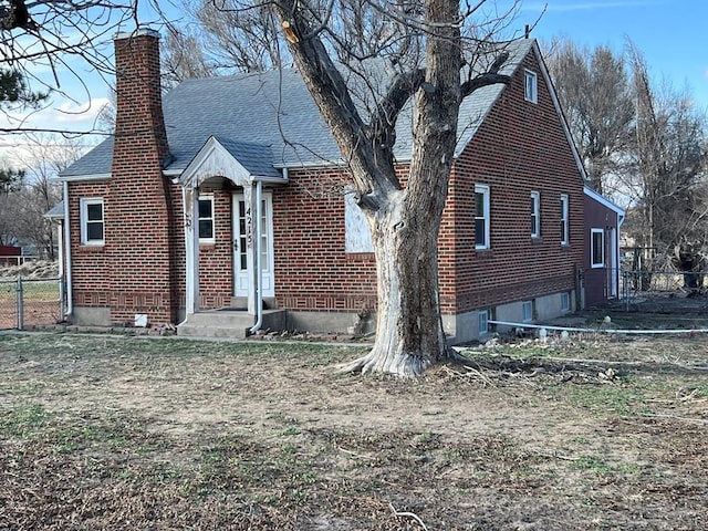 view of front of house featuring brick siding, a chimney, a shingled roof, fence, and a front lawn