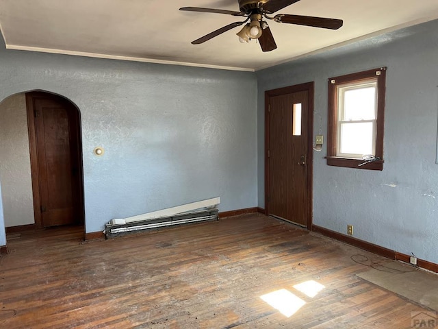 empty room featuring arched walkways, ceiling fan, baseboards, hardwood / wood-style floors, and crown molding