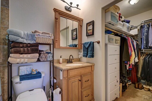 bathroom with a walk in closet, vanity, and toilet