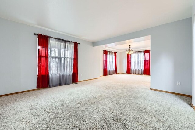 spare room featuring a chandelier, carpet flooring, and baseboards