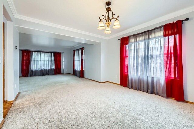 unfurnished room with an inviting chandelier, carpet, ornamental molding, and baseboards