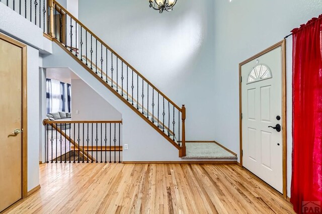 entrance foyer with stairway, light wood-type flooring, a towering ceiling, and baseboards