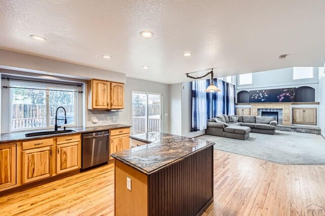 kitchen featuring a fireplace with raised hearth, stainless steel dishwasher, light wood-style floors, open floor plan, and a sink