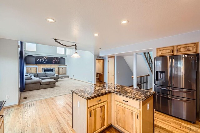 kitchen featuring stainless steel fridge, pendant lighting, open floor plan, and dark stone countertops