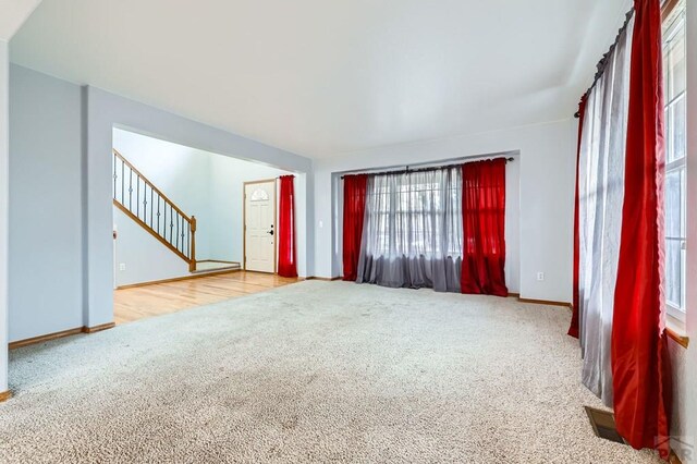 spare room featuring visible vents, light carpet, stairway, and baseboards