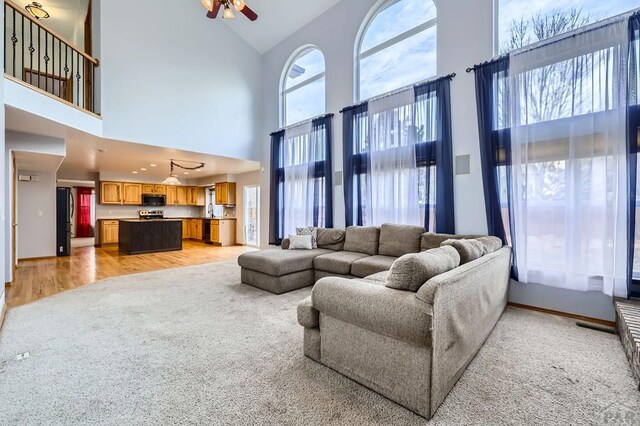 living room with a high ceiling, a ceiling fan, and light wood-style floors