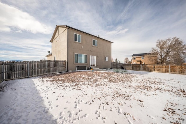 snow covered back of property featuring a fenced backyard and stucco siding