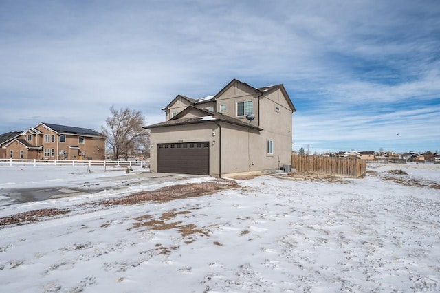 view of snow covered exterior with a garage, fence, and stucco siding