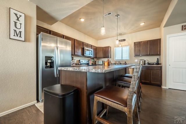 kitchen with decorative light fixtures, dark wood finished floors, appliances with stainless steel finishes, a kitchen island, and a kitchen breakfast bar