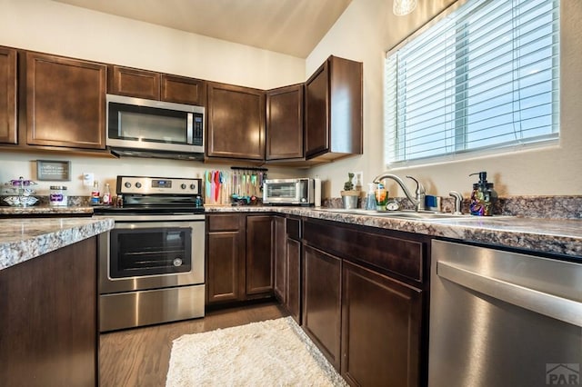 kitchen with appliances with stainless steel finishes, a sink, dark brown cabinets, and wood finished floors