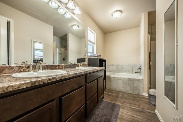 bathroom featuring double vanity, a garden tub, a sink, and wood finished floors