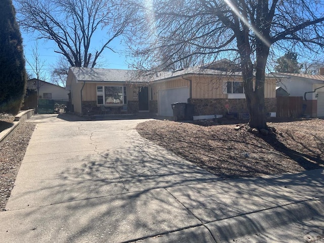 ranch-style home with concrete driveway, fence, stone siding, and a garage