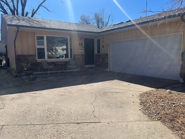 ranch-style house with concrete driveway, an attached garage, stone siding, and board and batten siding