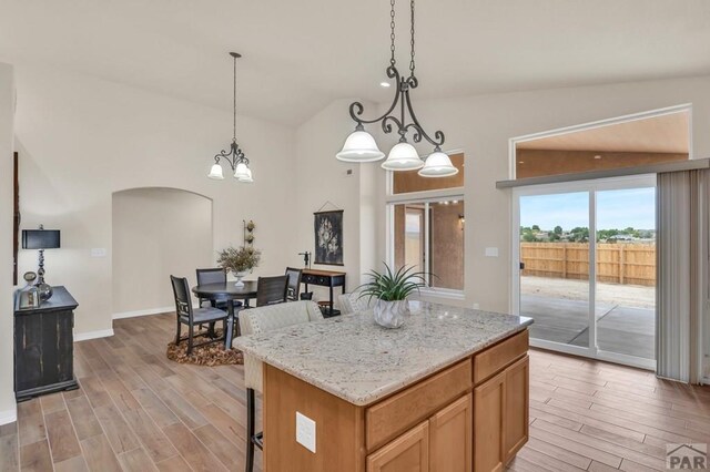 kitchen with hanging light fixtures, light wood-type flooring, arched walkways, and a center island