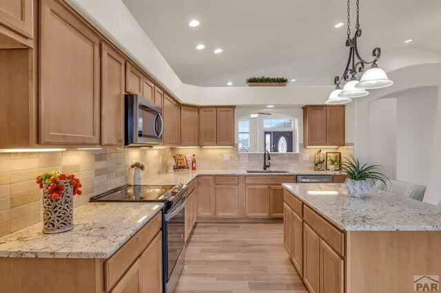 kitchen featuring lofted ceiling, appliances with stainless steel finishes, decorative light fixtures, a sink, and backsplash