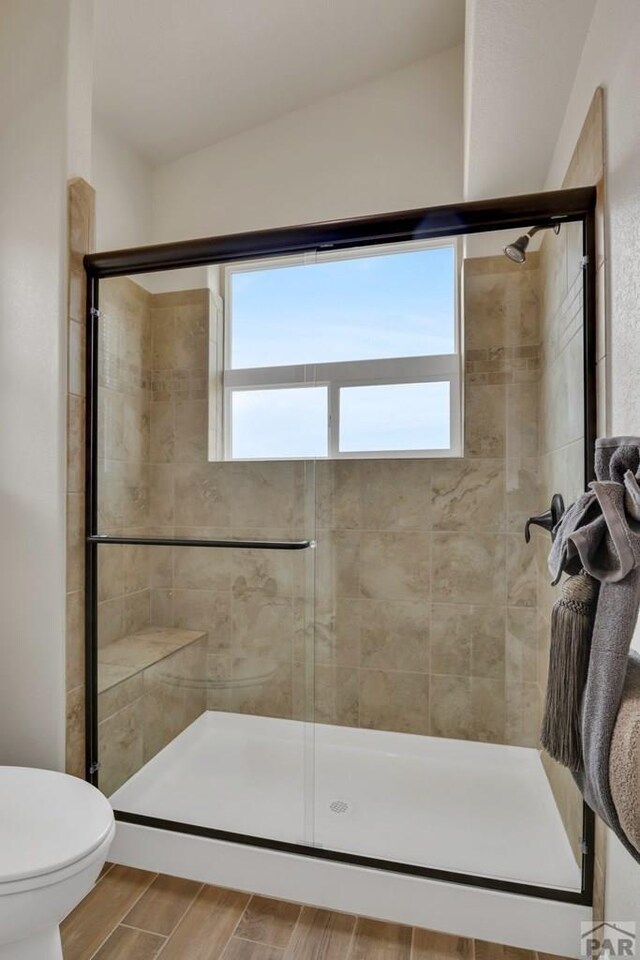 bathroom with vaulted ceiling, wood finish floors, a shower stall, and toilet