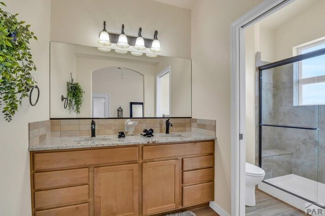 full bath with a stall shower, a sink, toilet, and double vanity