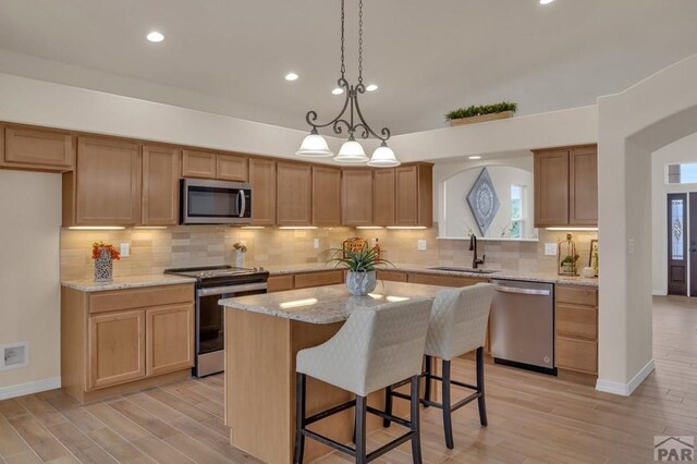 kitchen with a center island, arched walkways, appliances with stainless steel finishes, a sink, and light stone countertops