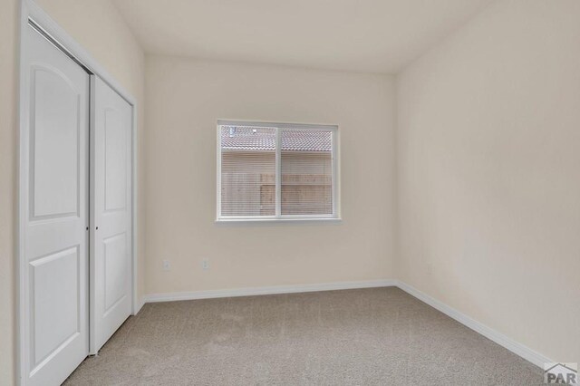 unfurnished bedroom featuring baseboards, a closet, and light colored carpet