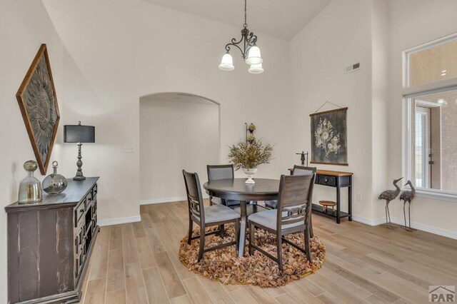 dining area with arched walkways, light wood finished floors, visible vents, high vaulted ceiling, and baseboards