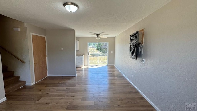 empty room featuring baseboards, a textured wall, wood finished floors, stairs, and a textured ceiling