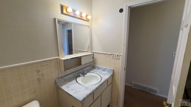 half bathroom with a wainscoted wall, vanity, visible vents, and tile walls