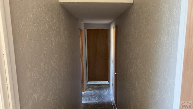 hall featuring a textured wall and a textured ceiling