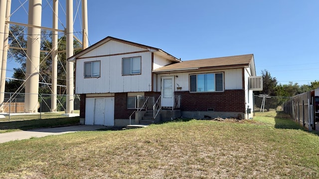 tri-level home featuring brick siding, a front lawn, and fence