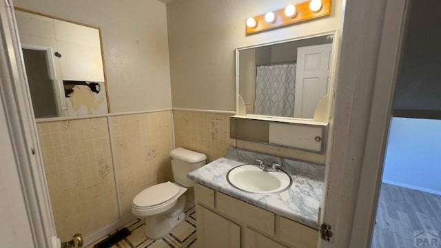 full bathroom featuring toilet, a wainscoted wall, tile walls, and vanity