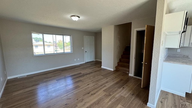 unfurnished room with a textured ceiling, wood finished floors, visible vents, baseboards, and stairway