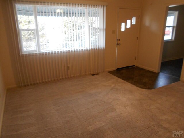 foyer entrance with a wealth of natural light, visible vents, and dark carpet