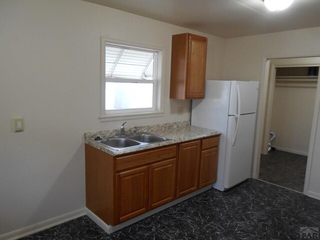 kitchen featuring marble finish floor, brown cabinetry, freestanding refrigerator, a sink, and baseboards