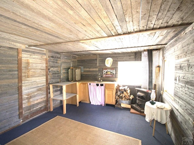 basement featuring carpet flooring, wooden walls, wooden ceiling, and a wood stove