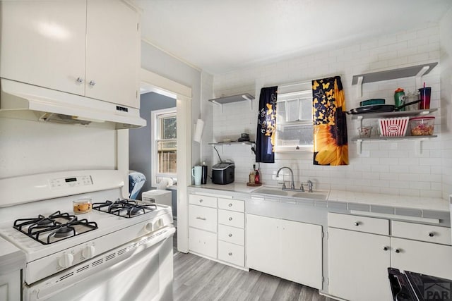 1908 E 5th St, Pueblo, CO 81001 - kitchen with white gas stove, under cabinet range hood, a sink, light wood-style floors, and decorative backsplash