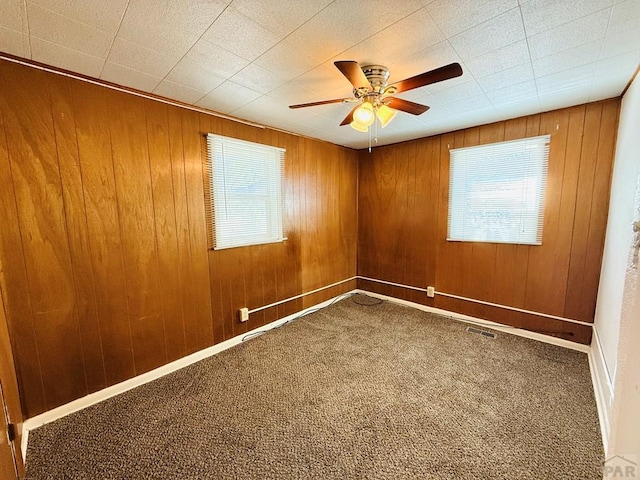 carpeted spare room with ceiling fan, wooden walls, visible vents, and baseboards