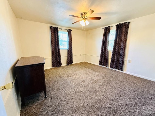 unfurnished bedroom with dark colored carpet, a ceiling fan, and baseboards