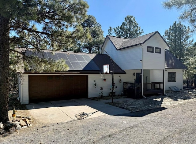 view of front of property featuring a garage, driveway, a shingled roof, and solar panels