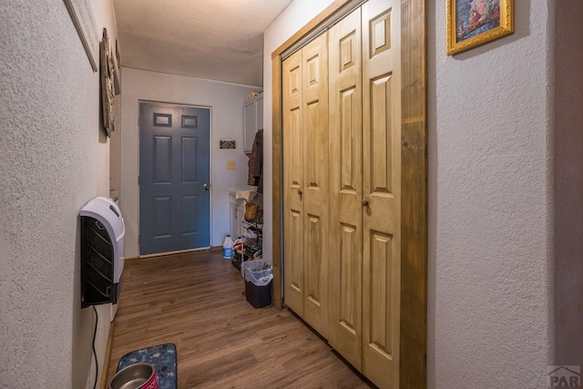 corridor featuring a textured wall, heating unit, and wood finished floors