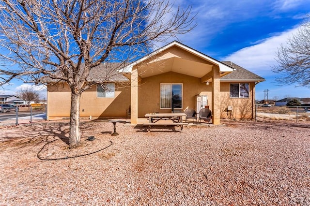 back of property with a shingled roof, fence, and stucco siding